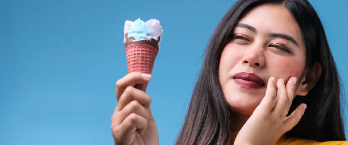 Young Asian woman with sensitive teeth and cold ice cream on color background